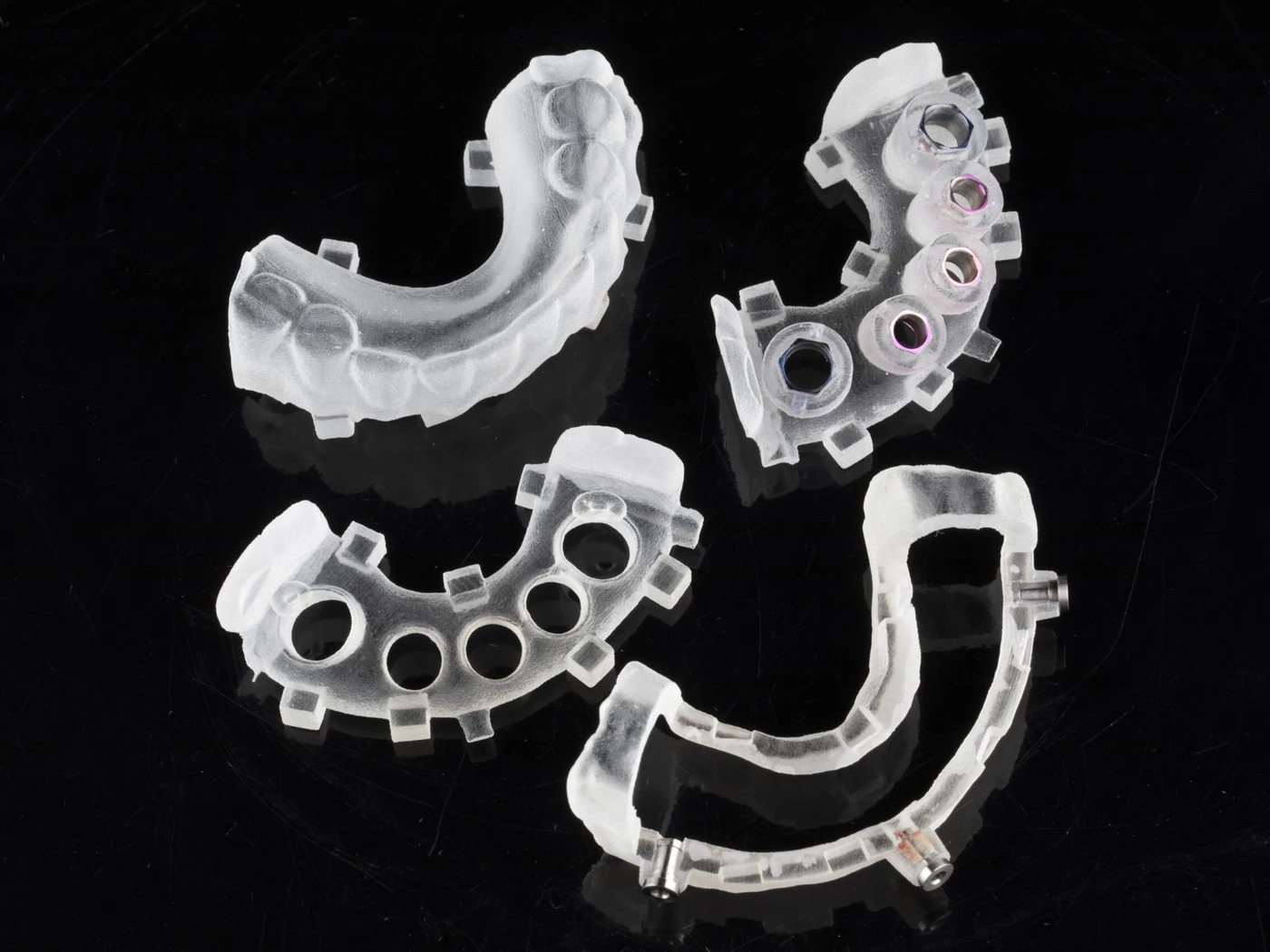 Four printed surgical guides on a black background — tooth-borne, bone-supported and bone-reduction types